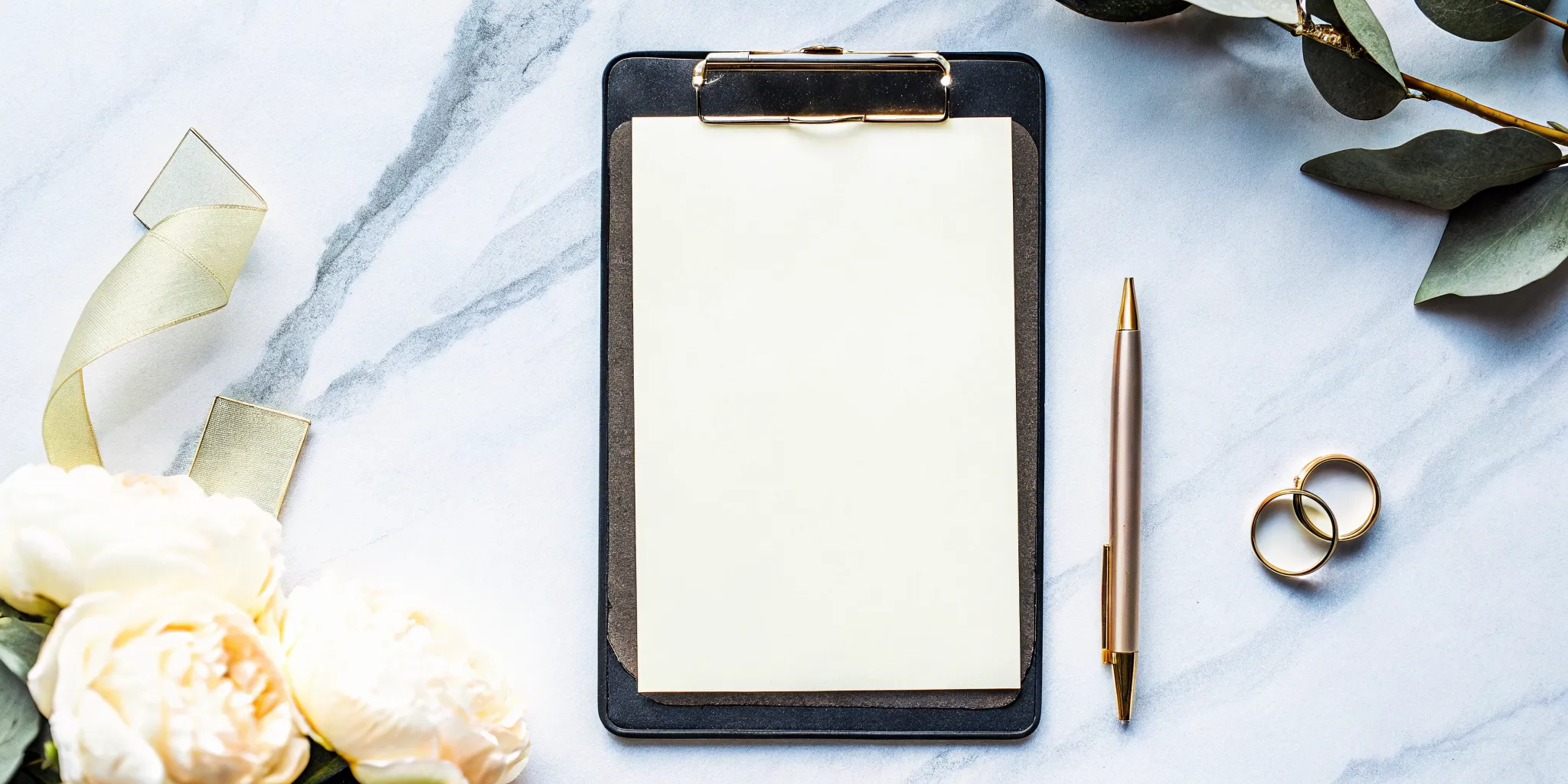 A wedding officiant script template on a clipboard with a pen, wedding rings, and white flowers.