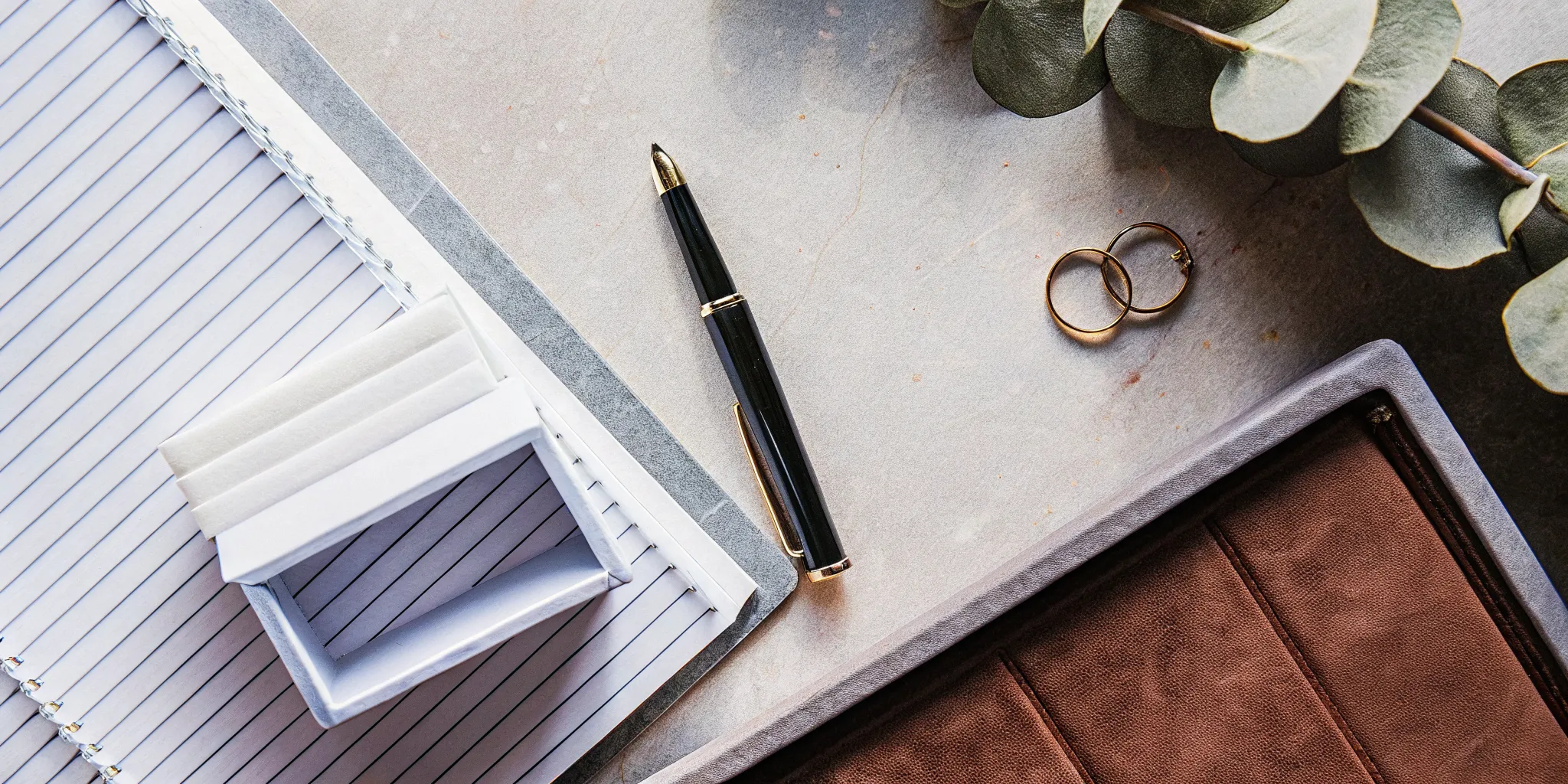 Writing a simple wedding officiant script in a notebook with wedding rings on the desk.