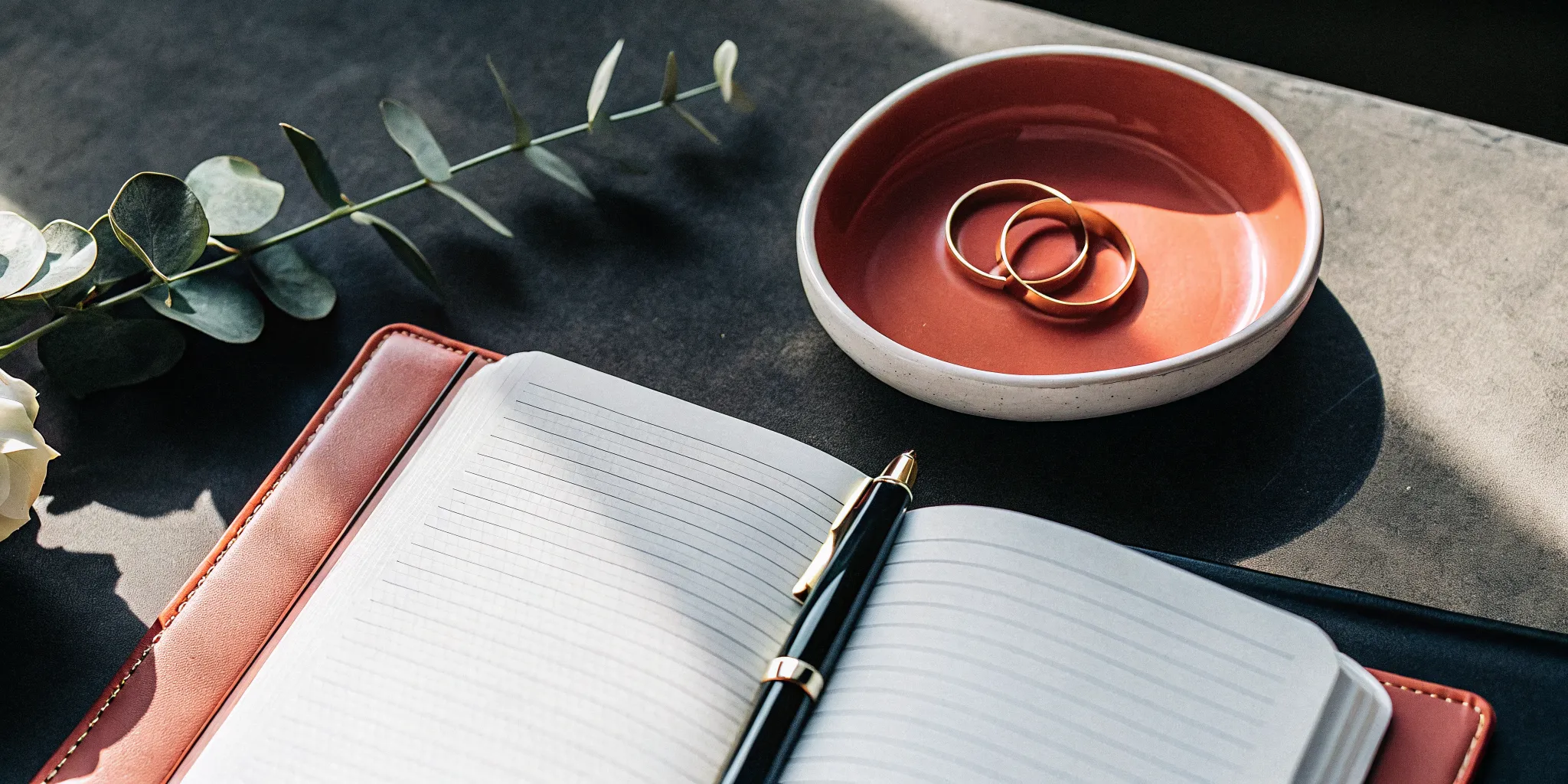 Writing a wedding ceremony script in a notebook with wedding rings nearby.
