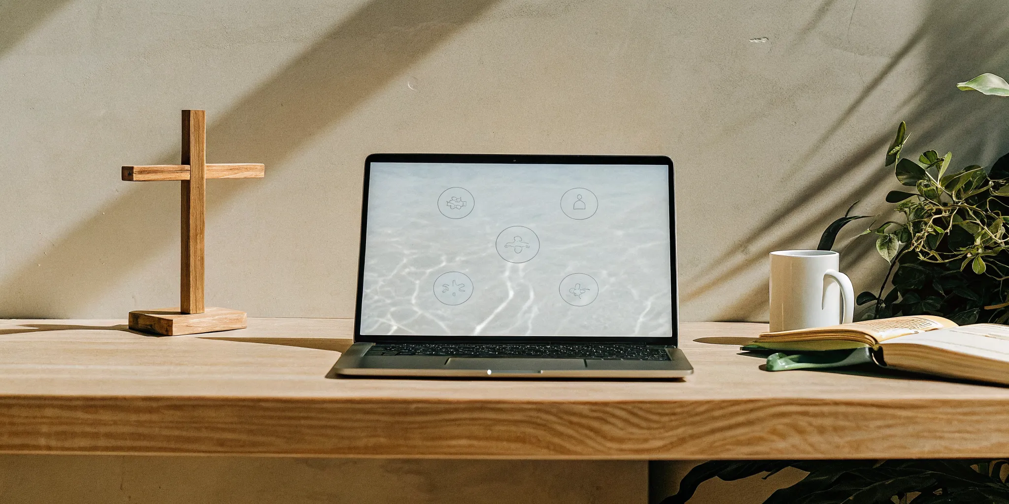 Getting a Baptist ordination online with a laptop, open book, and cross on a desk.