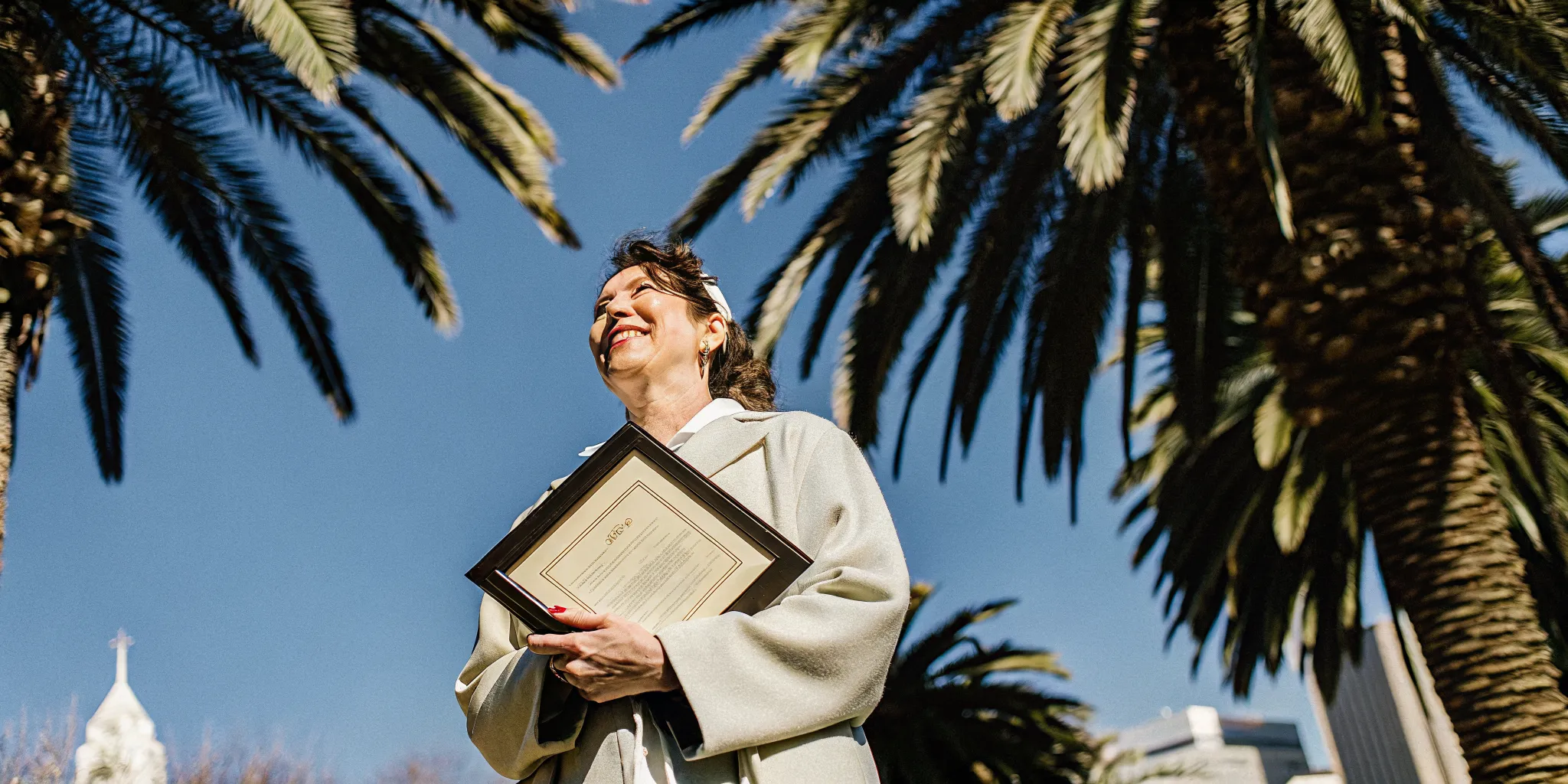Newly ordained minister holding a certificate of ordination with palm trees and the Orlando skyline softly blurred in the background