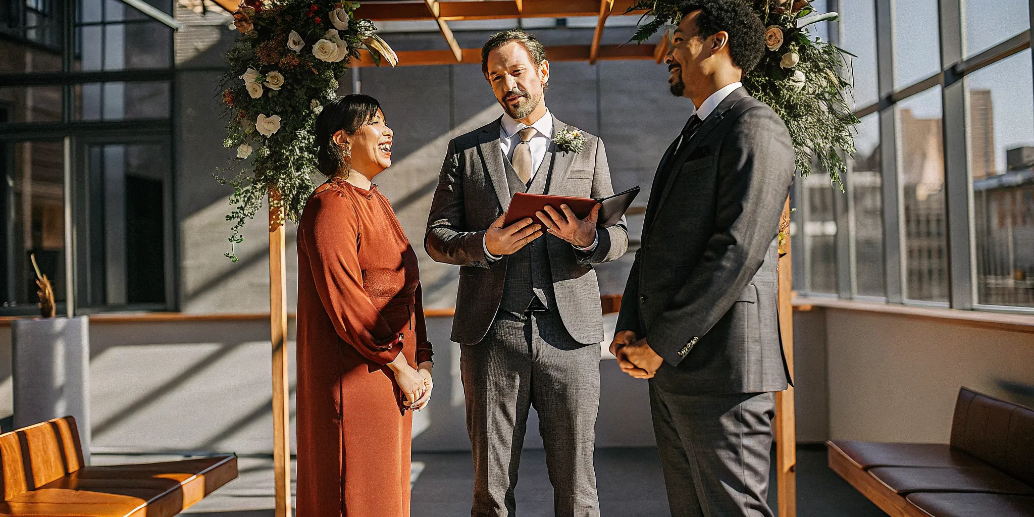 A great wedding officiant leads a joyful ceremony for a couple under a floral arch.