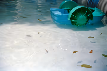 Close-up of a shallow clear water pool with scattered leaves and part of a green paddle wheel boat visible at the top right.