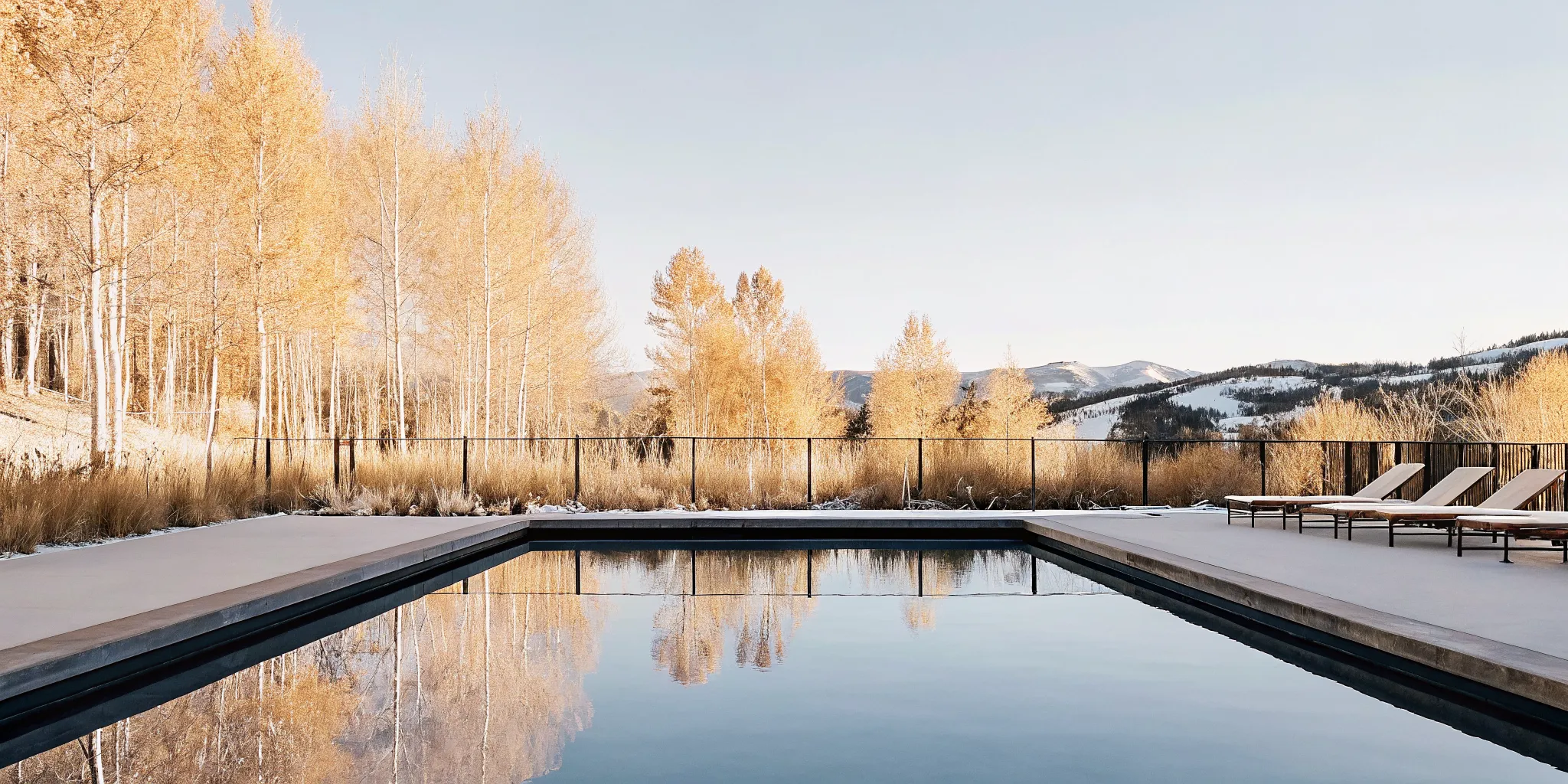 A beautiful backyard swimming pool in Colorado with autumn colors on the surrounding trees, mountains in the distance, crisp natural lighting