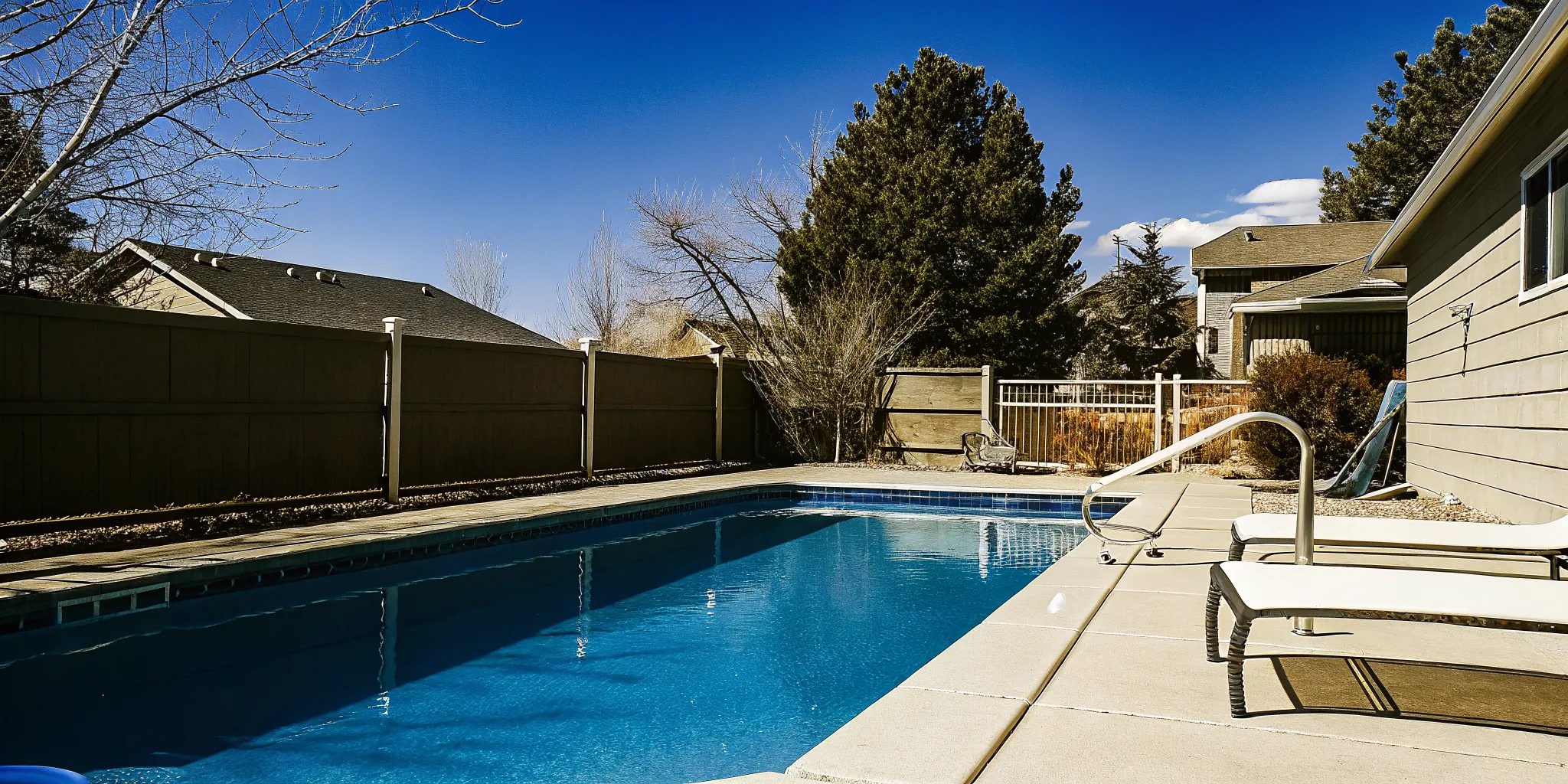A pristine backyard swimming pool in Denver, Colorado, sparkling crystal clear water under the sunny blue sky, with Rocky Mountains in the far background.