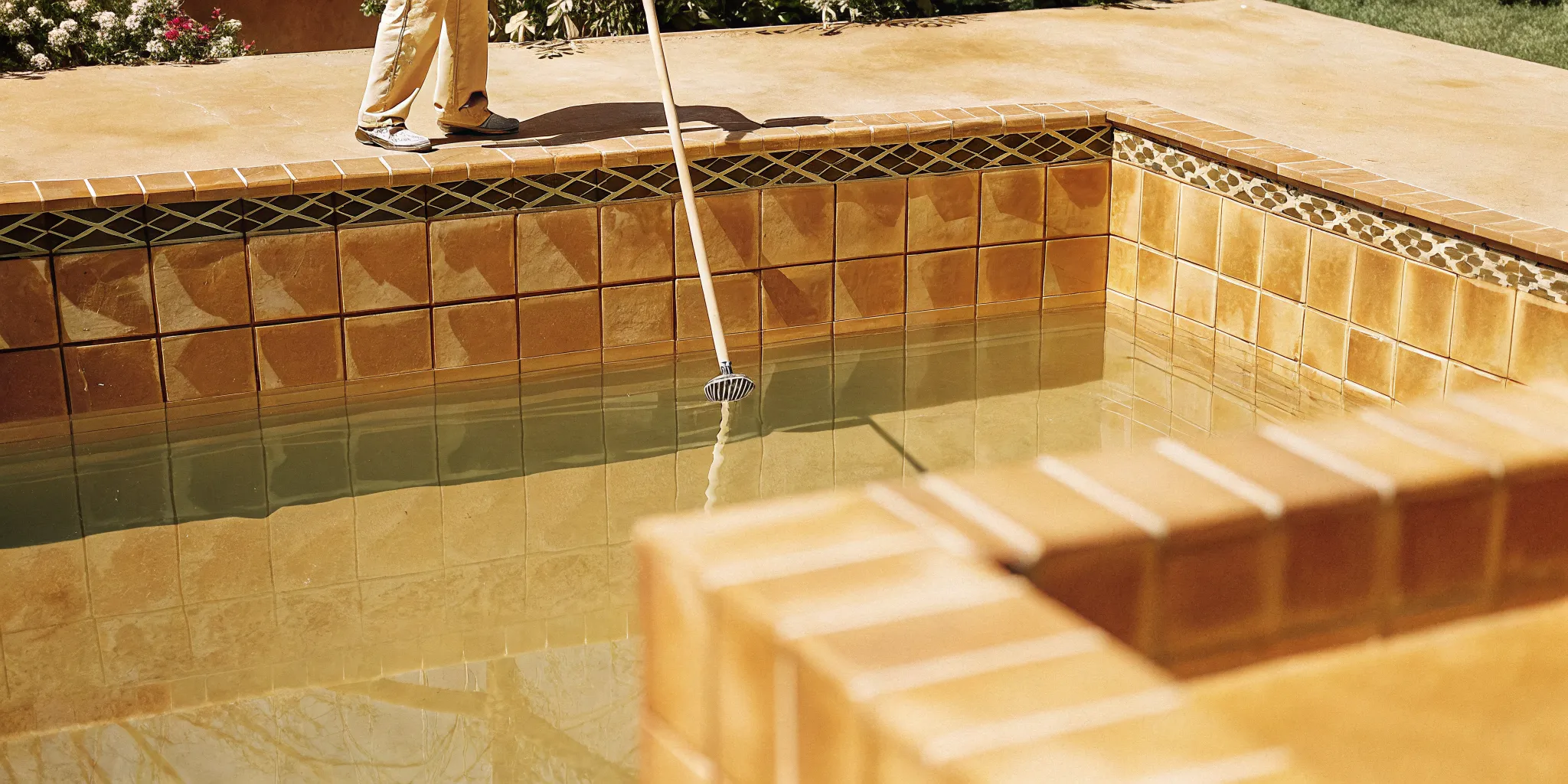 A professional pool technician brushing the tiles of a beautiful clean swimming pool in Denver Colorado