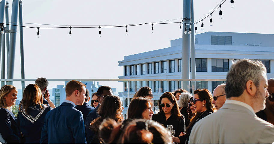 Group of business people socializing on an outdoor terrace with modern buildings in the background.