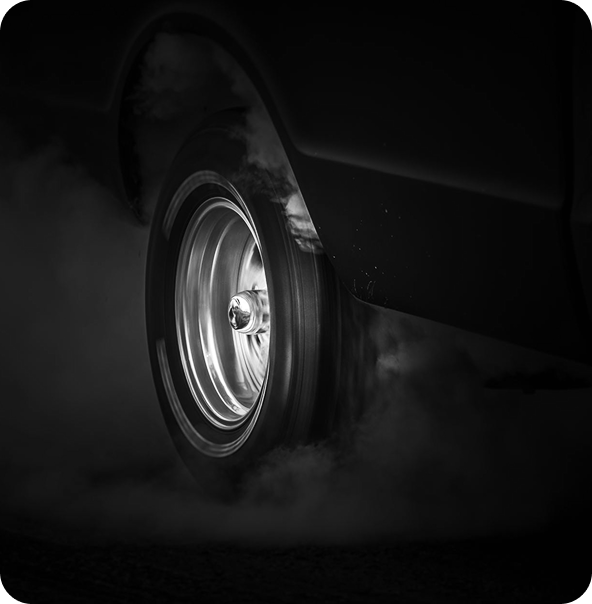 Close-up of a car tire spinning fast, creating smoke around it on a dark surface.