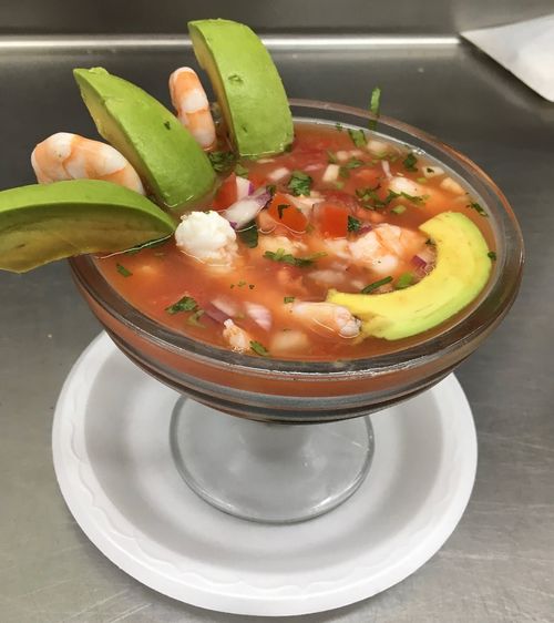 A bowl of soup with shrimp, avocado, and lime.
