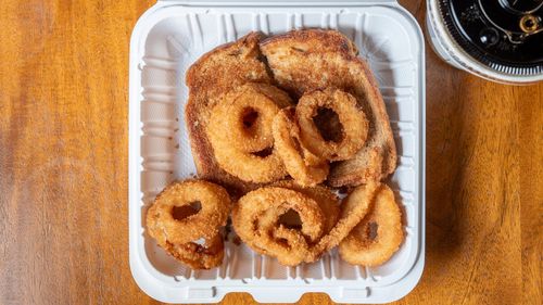 A white paper plate with a sandwich and onion rings on it.