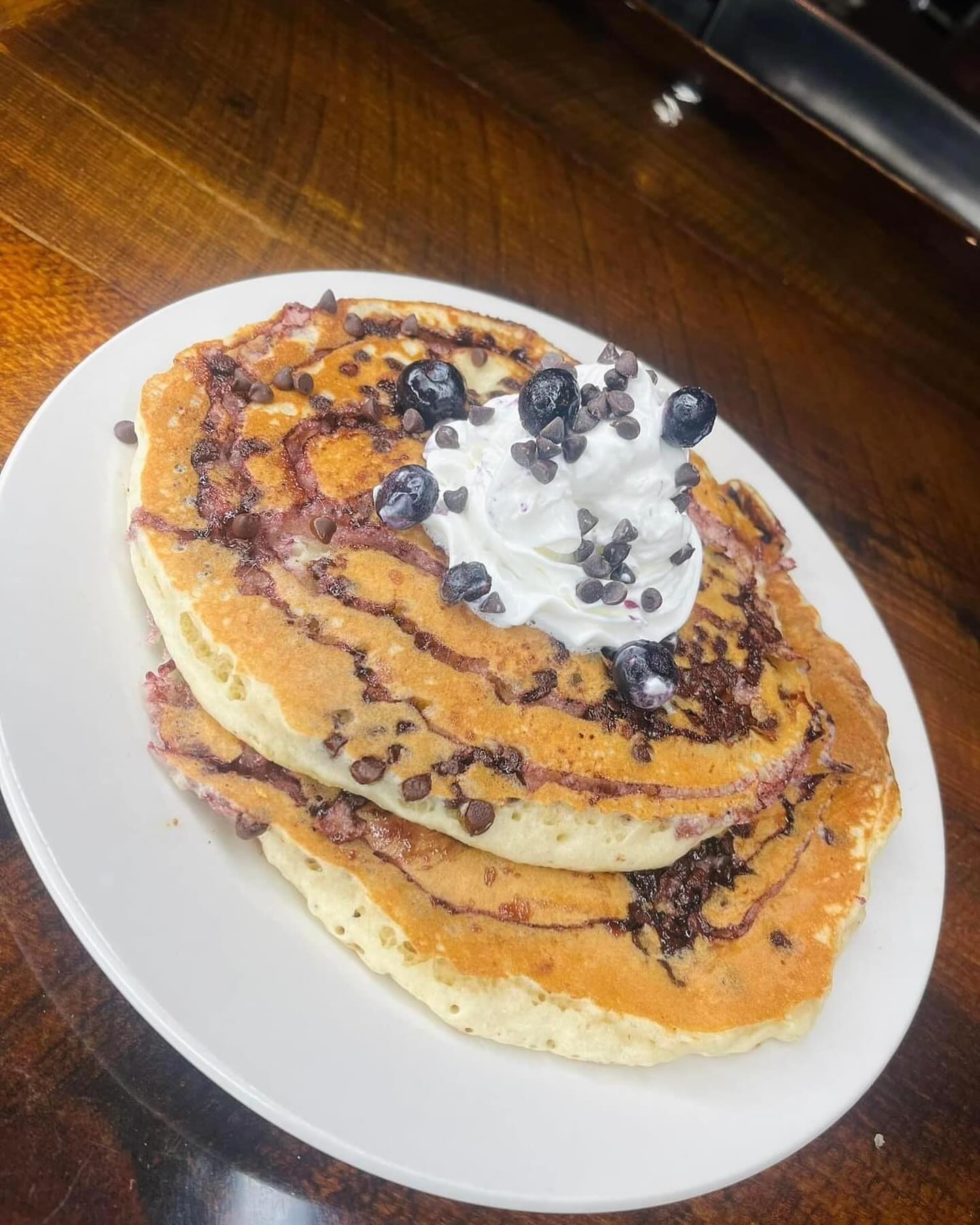 Stack of blueberry pancakes with chocolate chips, topped with whipped cream and fresh blueberries on a white plate.