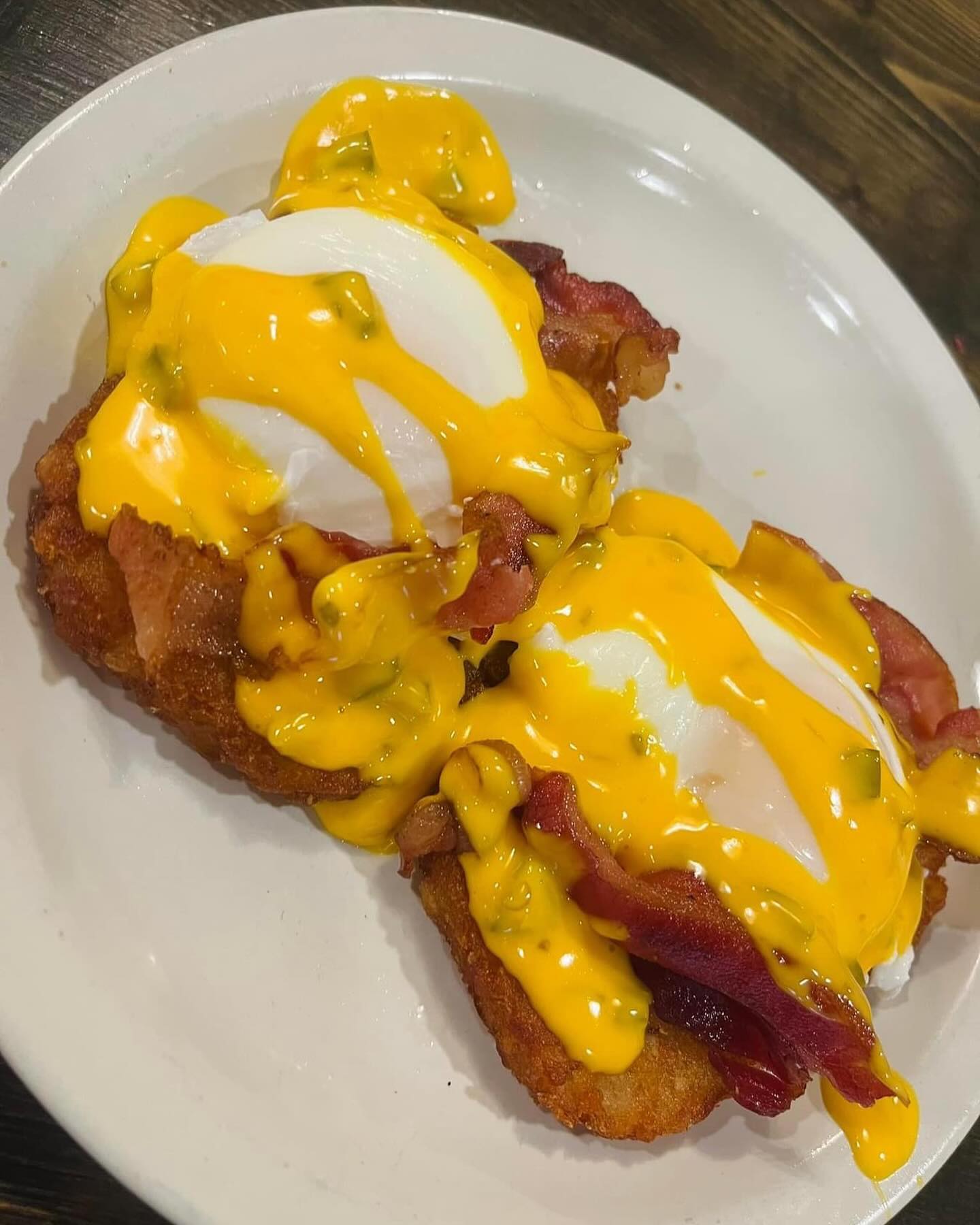 Two poached eggs with cheese sauce and bacon on crispy hash brown patties on a white plate.
