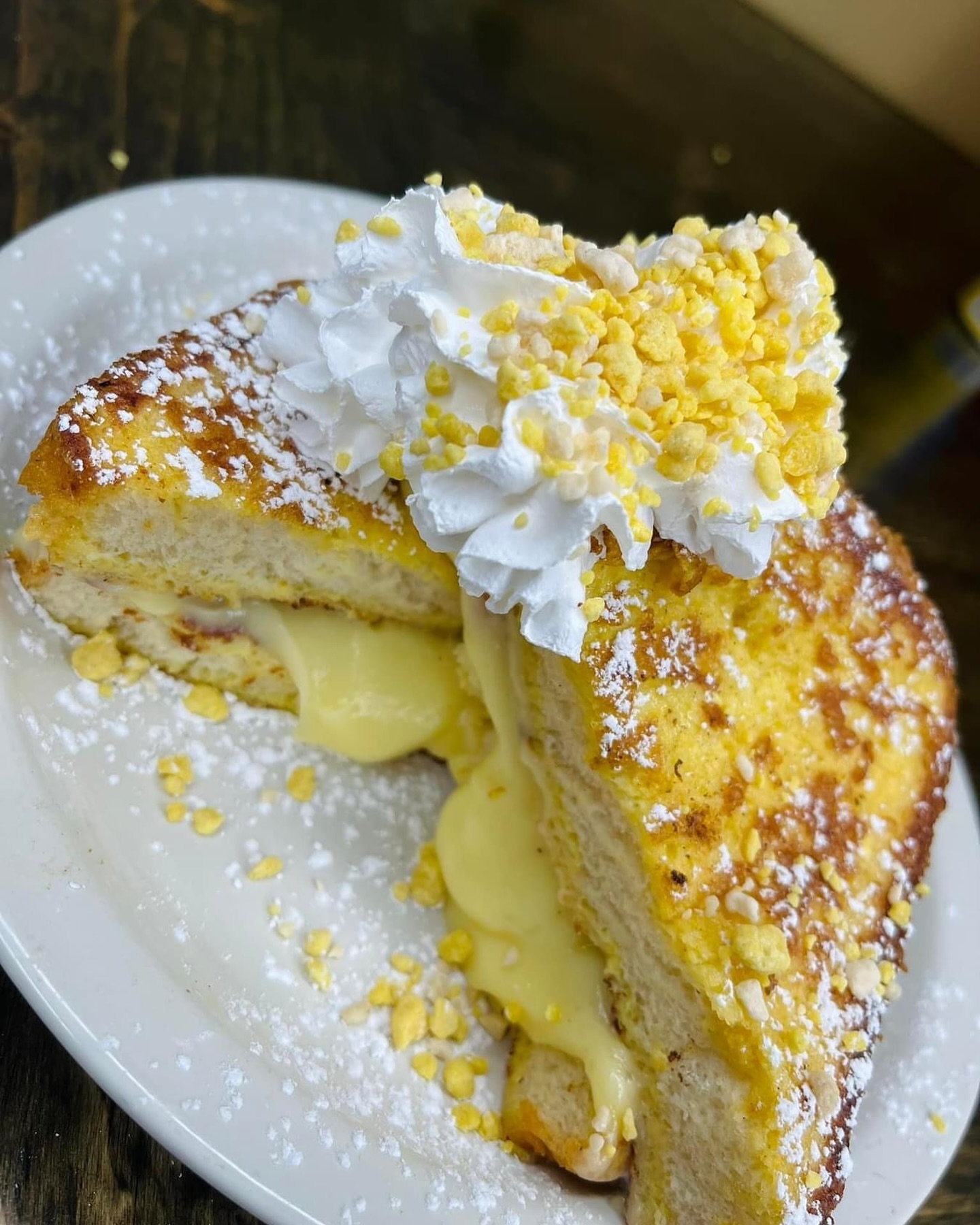 Slice of French toast filled with creamy custard, topped with whipped cream and yellow crunchy sprinkles on a white plate.