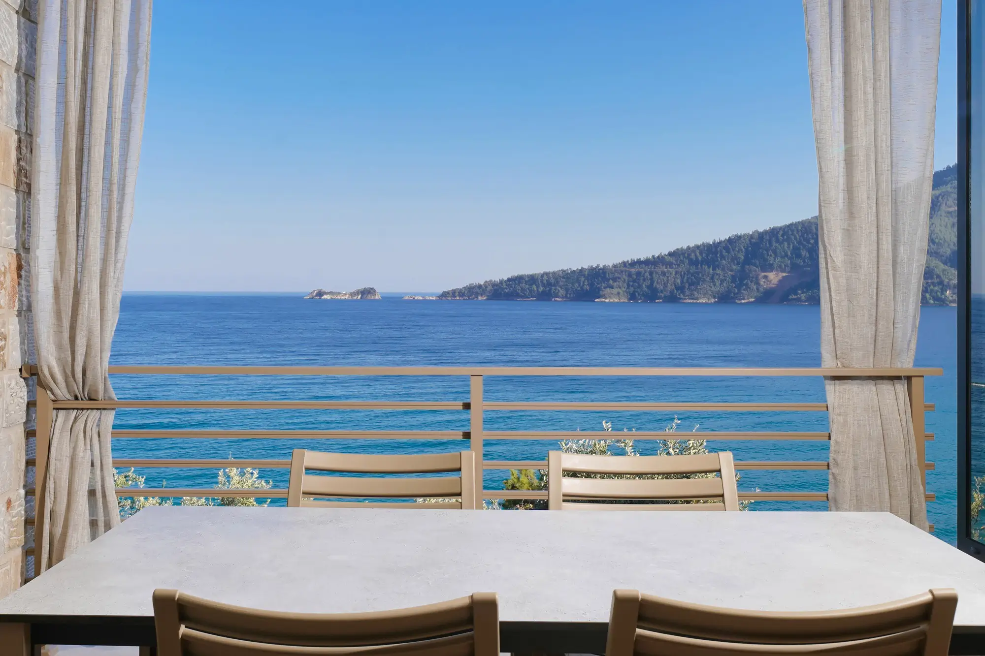 Terrace dining table framed by linen curtains with panoramic Aegean bay view | Terrace