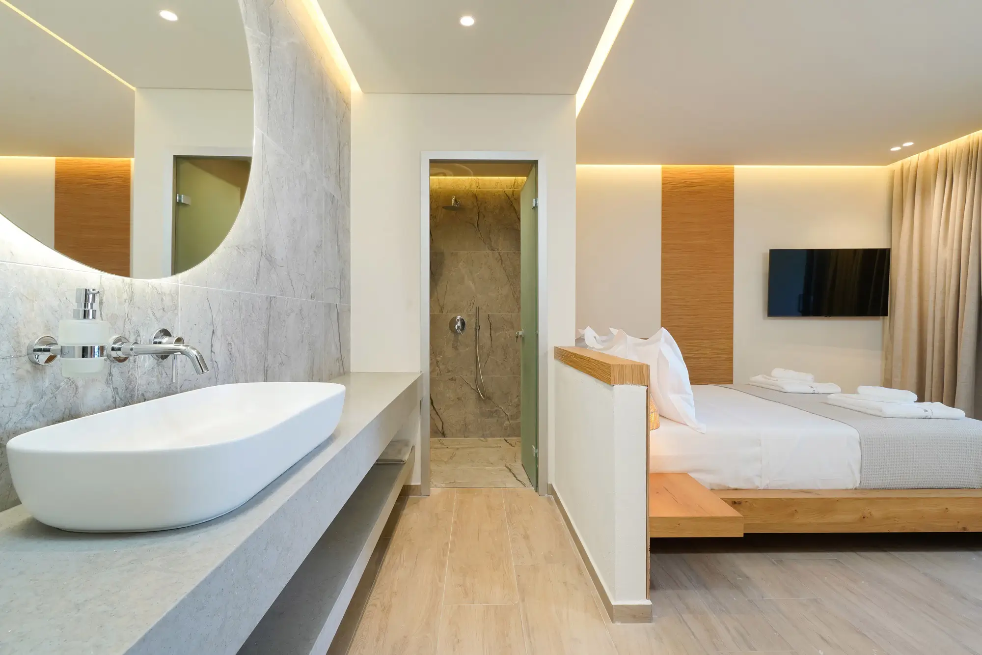 Marble vessel sink with backlit round mirror and walk-in shower beyond | Bathroom