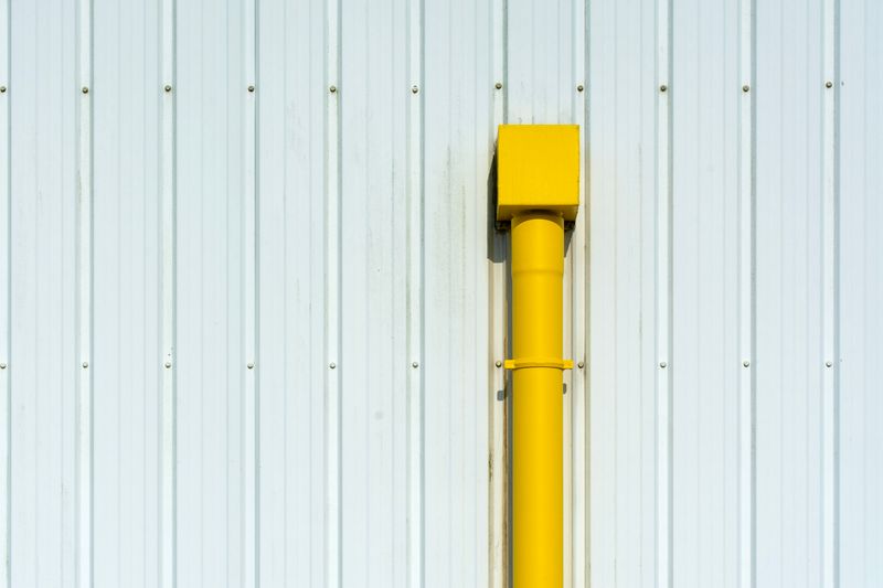 A vibrant yellow pipe stands out against a white corrugated metal wall, creating a striking contrast.