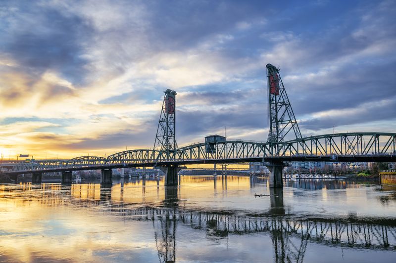 Picturesque scenery of aged Hawthorne Bridge crossing calm river reflecting cloudy sunset sky in Portland