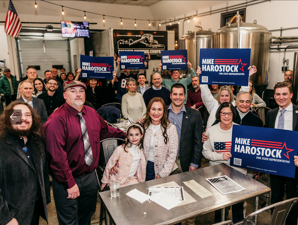Group of people gathered in a brewing company holding blue campaign signs for Mike Harostock for State Representative.