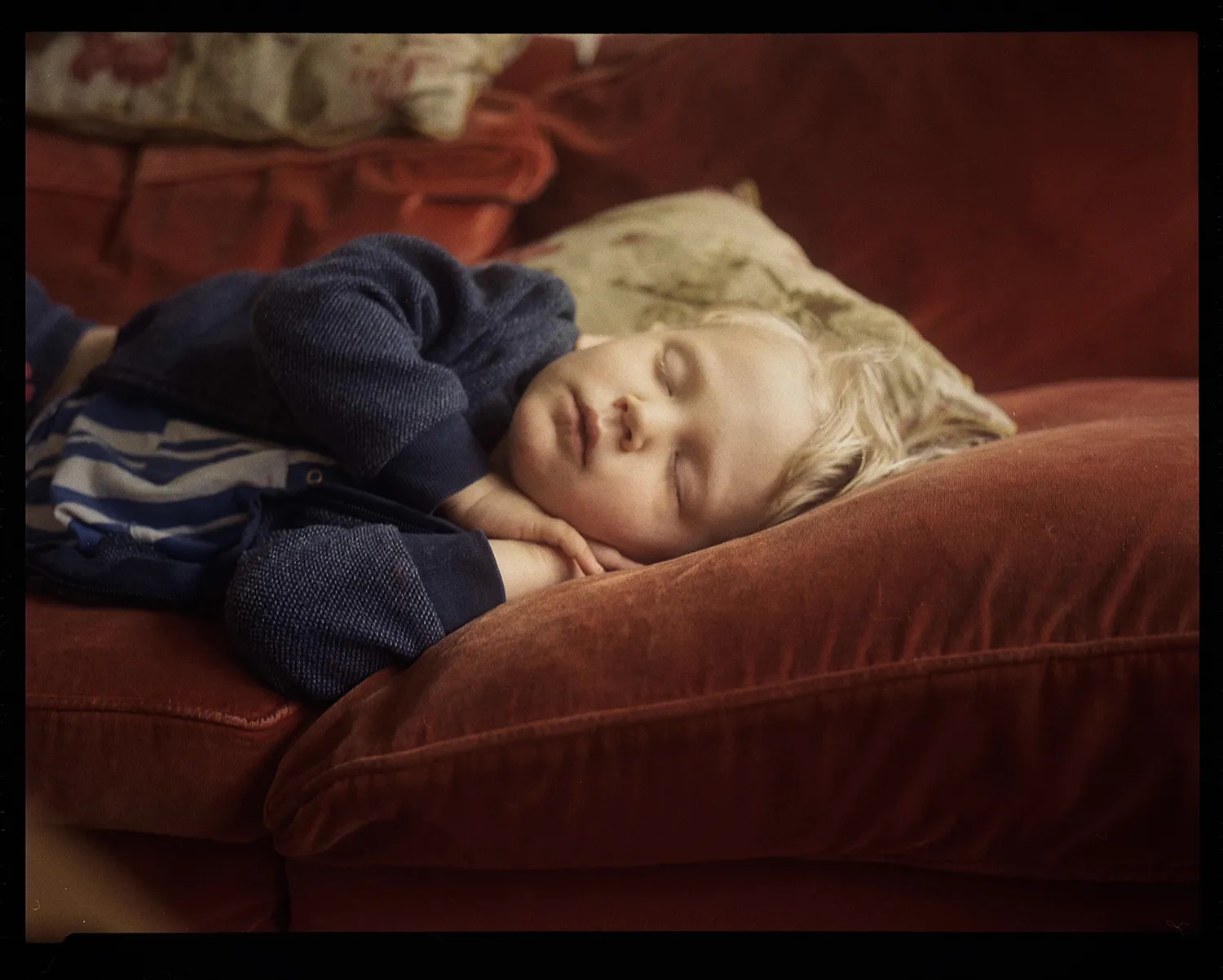 Young child peacefully sleeping on a red velvet couch with head resting on a pillow.