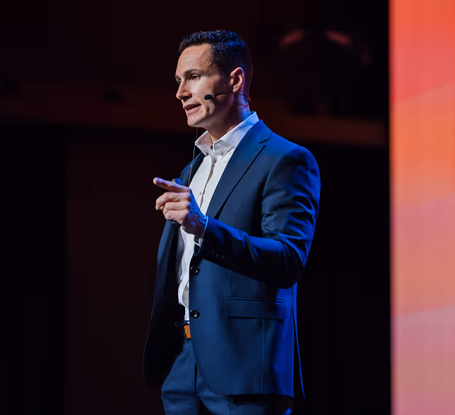 Three men in suits conversing near a bar counter with various bottles and cups, in a social or networking event setting.