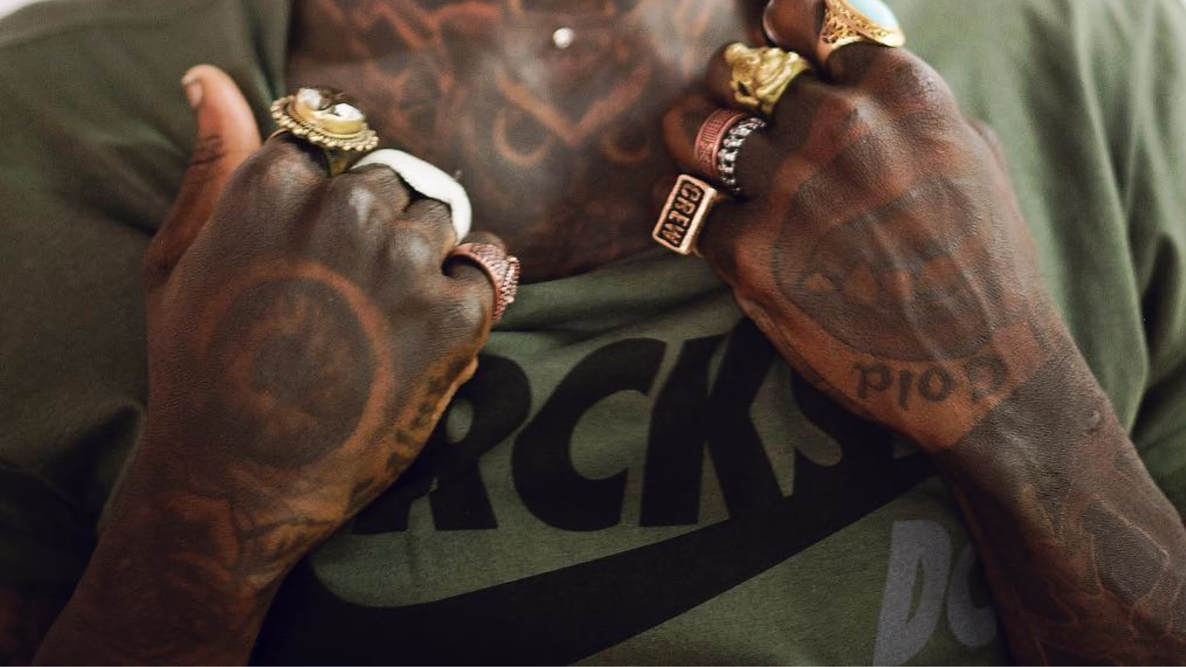 Close-up of tattooed hands with rings over a Ruckus shirt