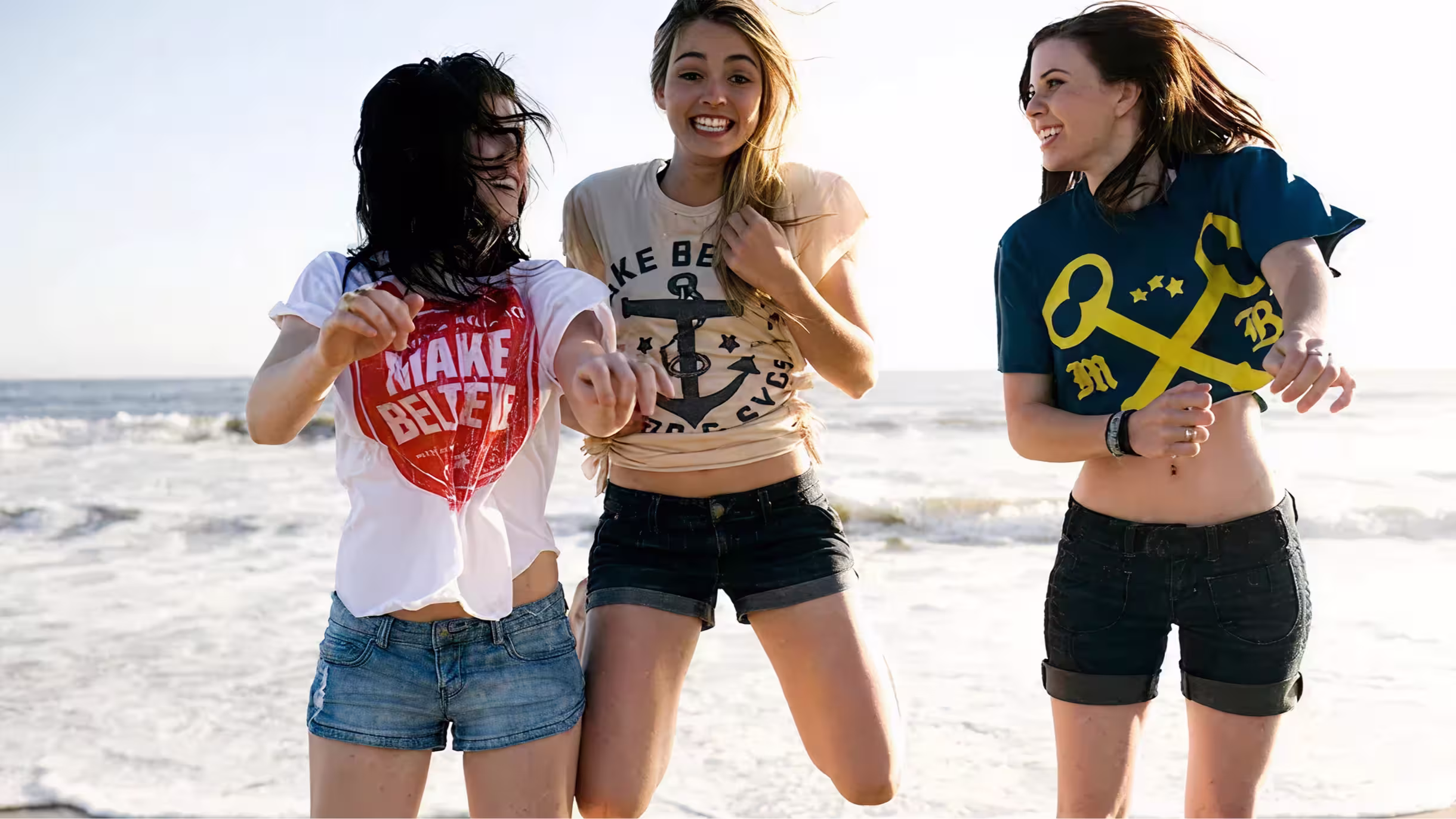 Three women wearing Make Believe T-shirts at the beach