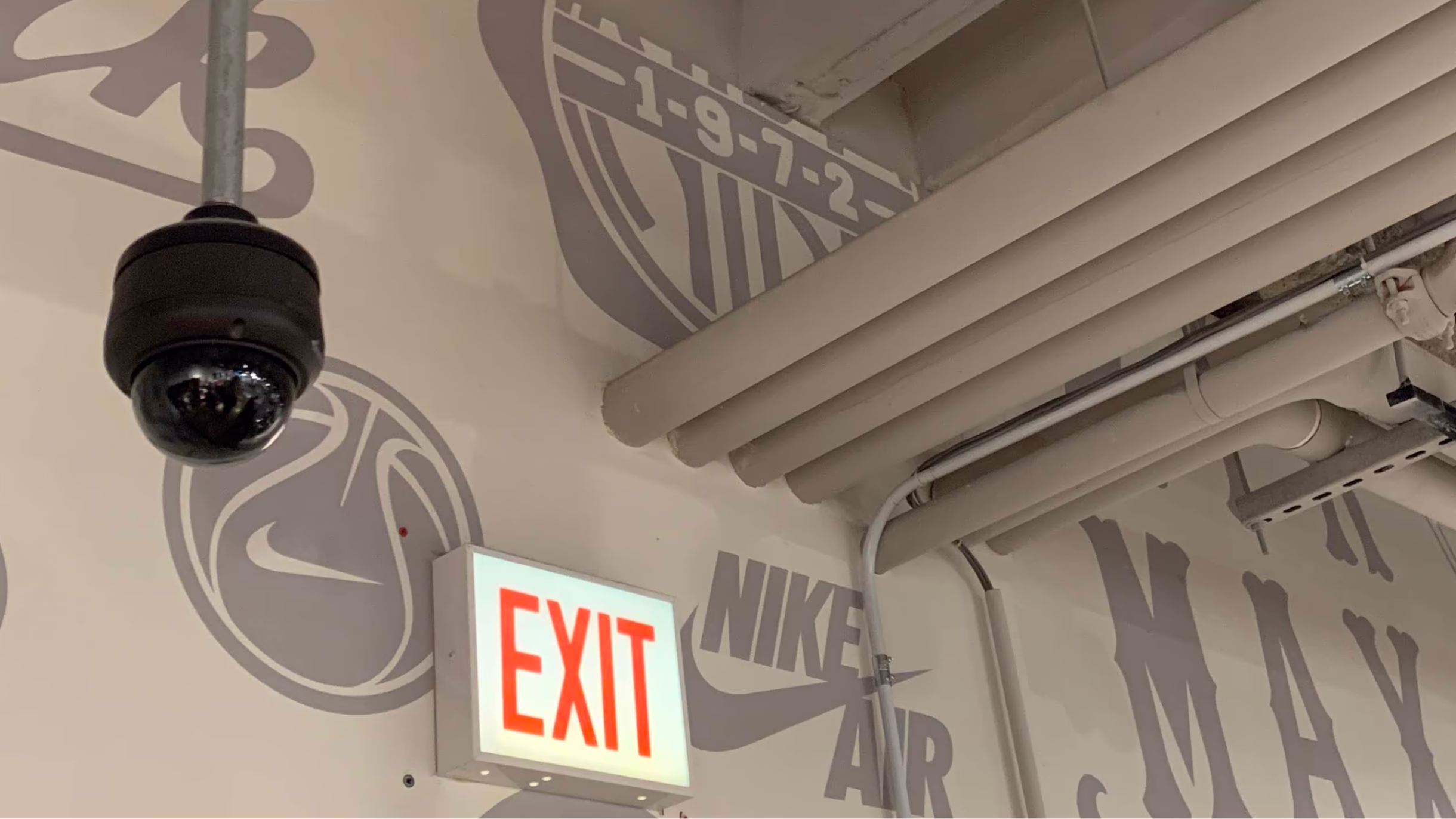Security camera and exit sign surrounded by the Nike Chicago mural