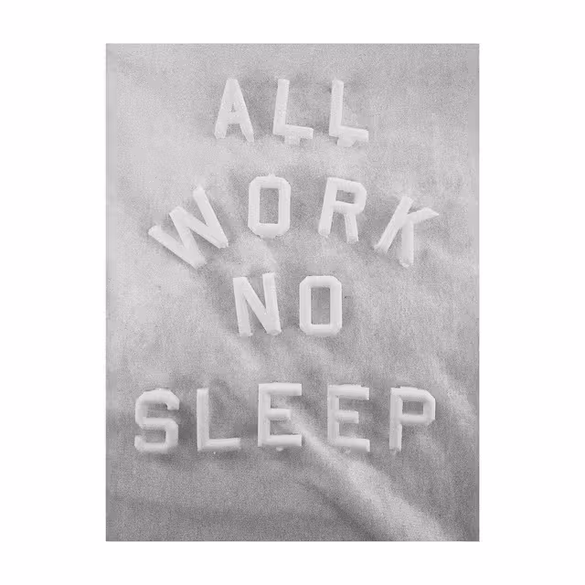 Black-and-white photograph of raised letters spelling “ALL WORK NO SLEEP”