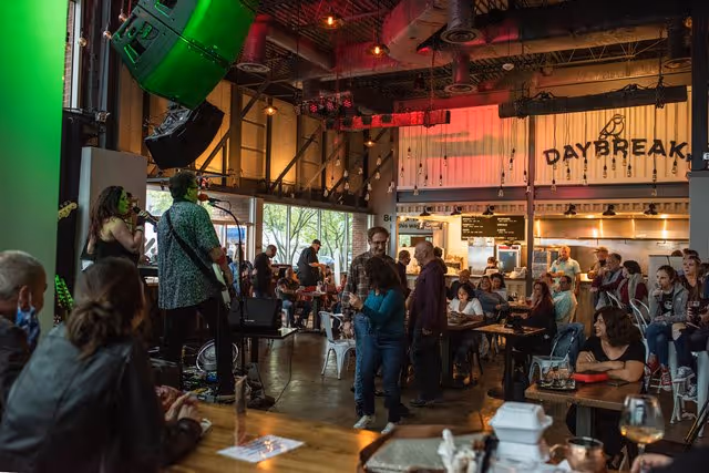 A live band performs inside a bustling restaurant, with patrons sitting and standing, enjoying food and music.