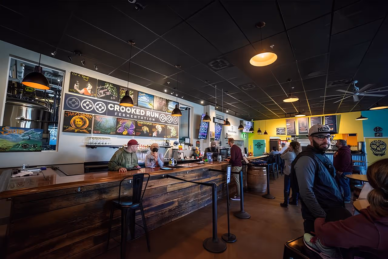 Interior of Crooked Run Fermentation with patrons at the wooden bar and brewing tanks visible in the background.