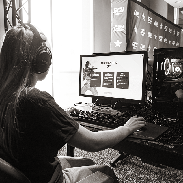 Person with long hair wearing headphones, using a computer with a game screen titled 'State of Play Premier' displayed.