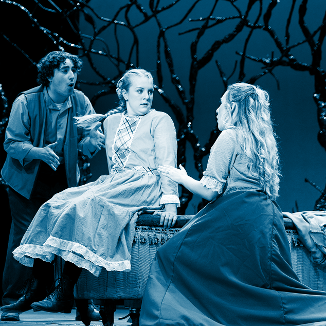Three actors in period costumes performing a dramatic scene on stage with bare tree branches in the background.