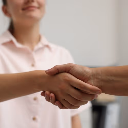 Two people shaking hands, with one person smiling in the background.