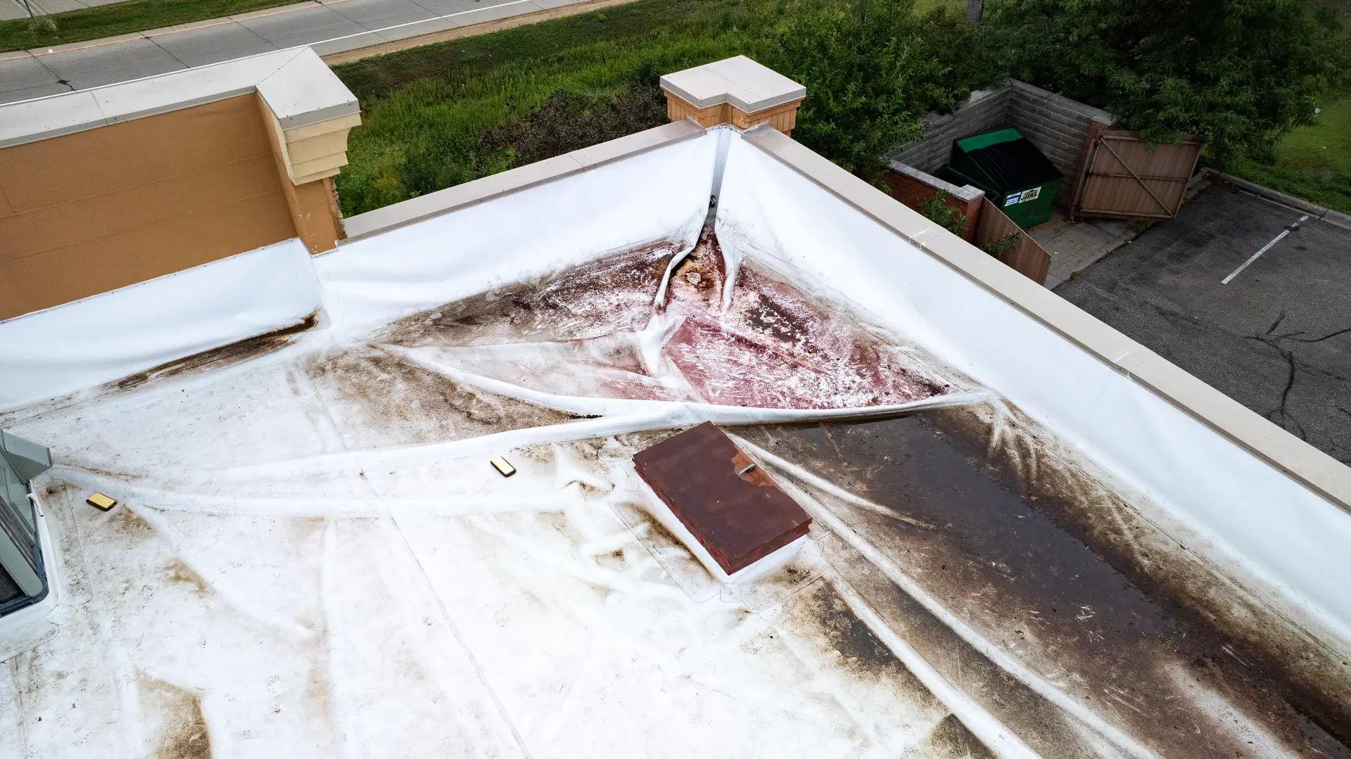 White flat roof with visible dirt, stains, and debris, alongside a small brown rectangular vent.