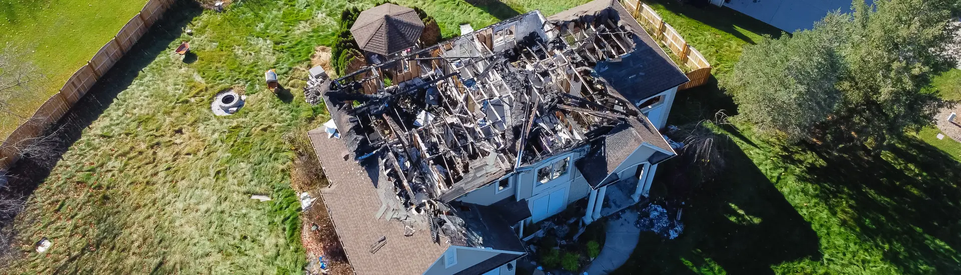 Aerial view of a house with extensive fire damage to the roof, showing charred and collapsed wooden beams.