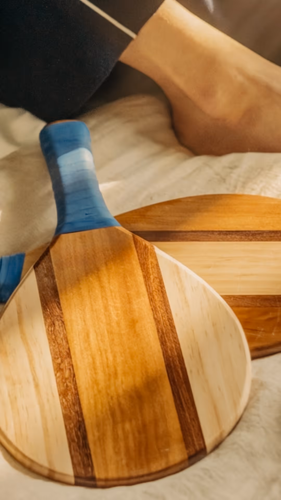 Raquette de ping-pong en bois avec poignée bleu, posée sur un tissu clair avec une autre raquette en arrière-plan.