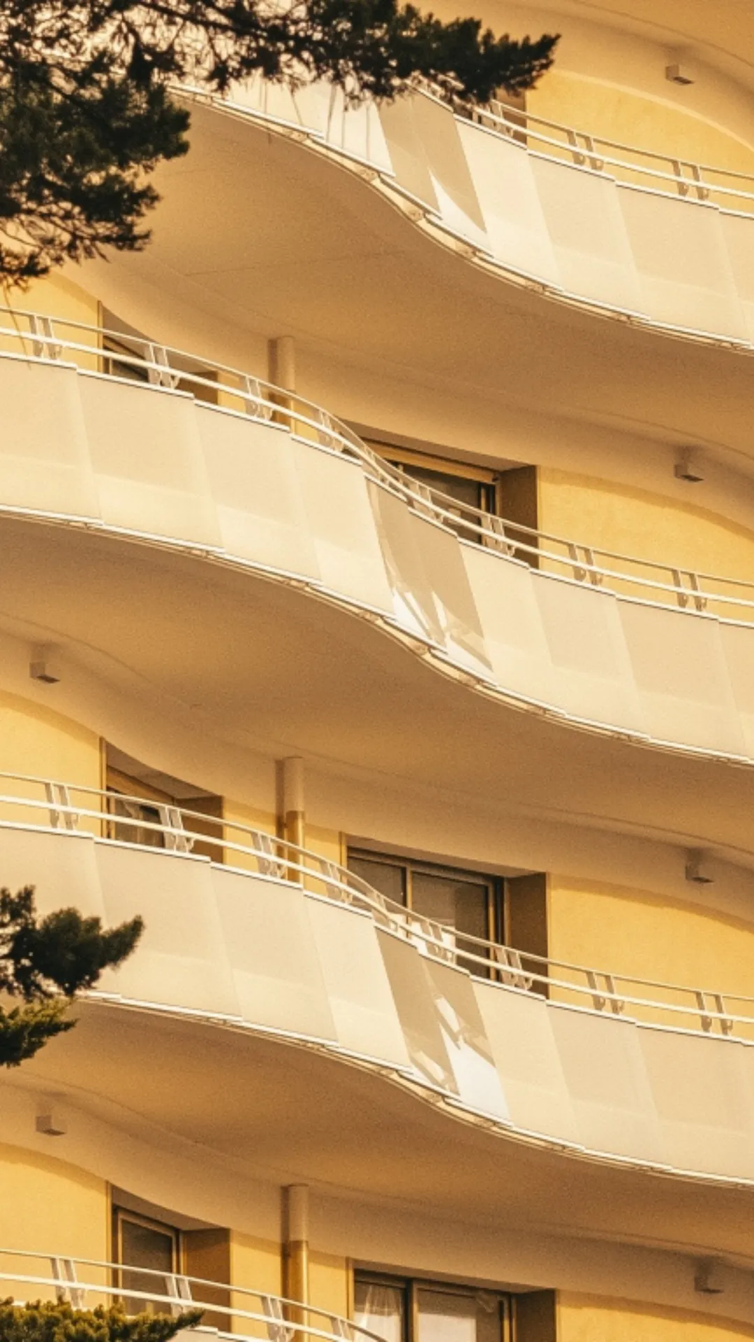 Façade d'immeuble avec balcons courbés en blanc et murs jaunes sous un ciel clair.