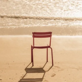 Chaise rouge seule sur la plage sablonneuse avec l'océan brillant en arrière-plan.