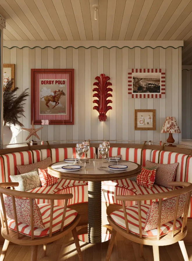 Coin repas élégant avec banquette arrondie à rayures rouge et blanc, table en bois ronde dressée avec assiettes et verres, décor mural avec affiches et lampe à motif rouge.