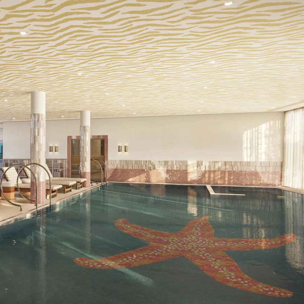 Piscine intérieure avec un grand motif en forme d'étoile de mer au fond, plafond à motifs ondulés et chaises longues sur le côté.