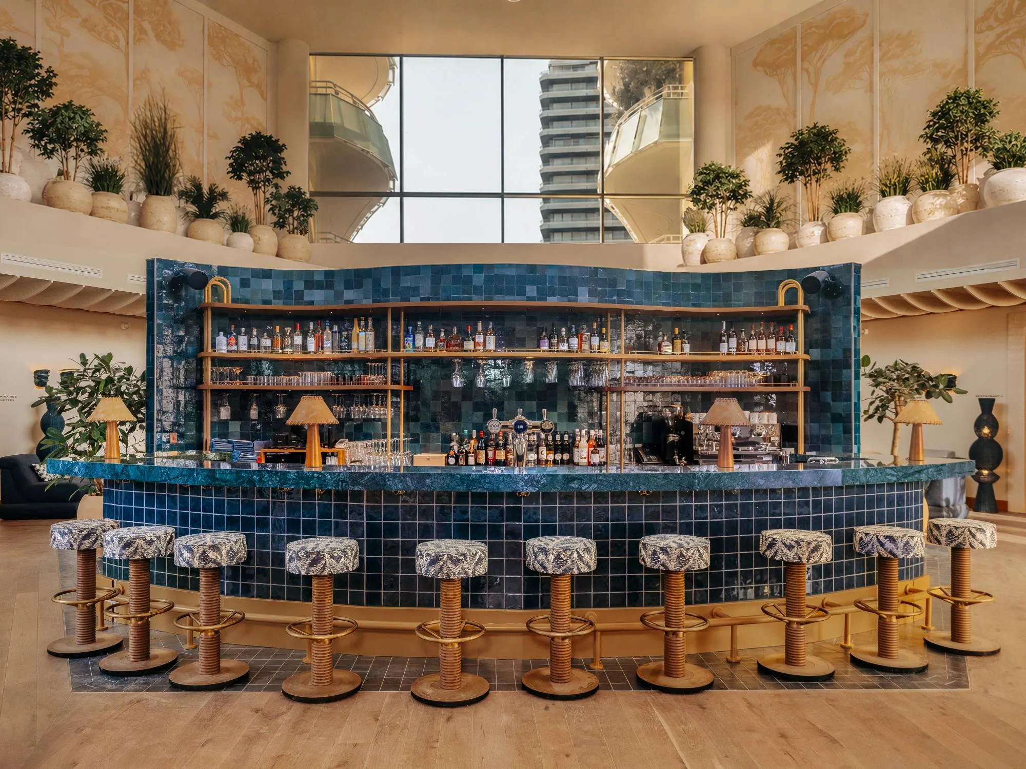 Bar avec tabourets en bois à hauteur réglable et carrelage bleu, plantes et lampes décoratives.