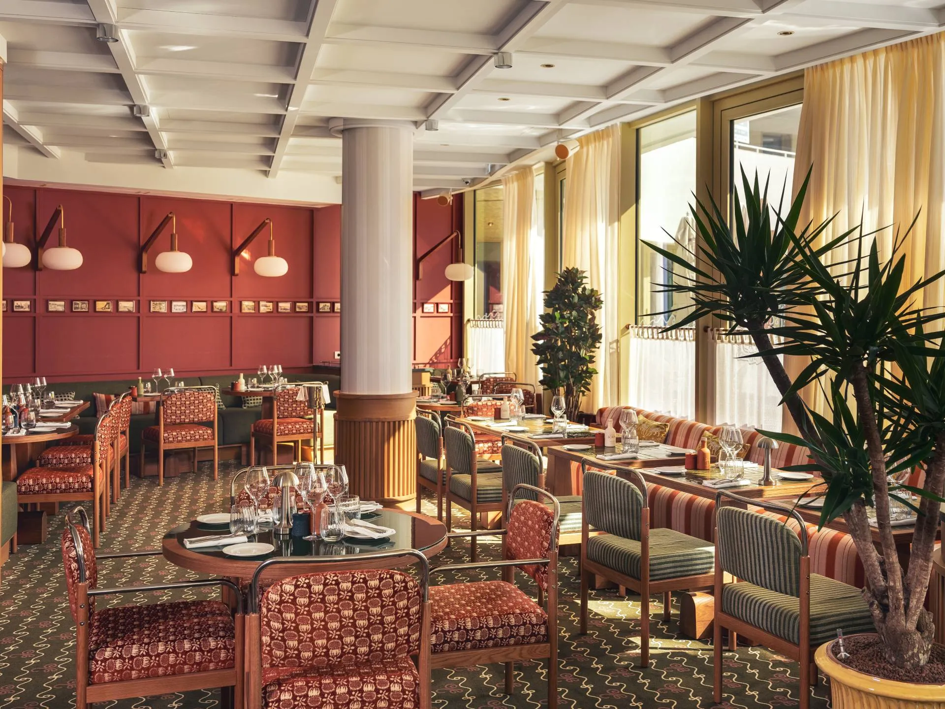 Intérieur lumineux de restaurant avec tables élégamment dressées et chaises colorées près de grandes fenêtres.
