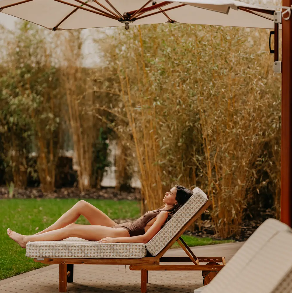 Woman in a swimsuit lying on a deckchair outside under a parasol.