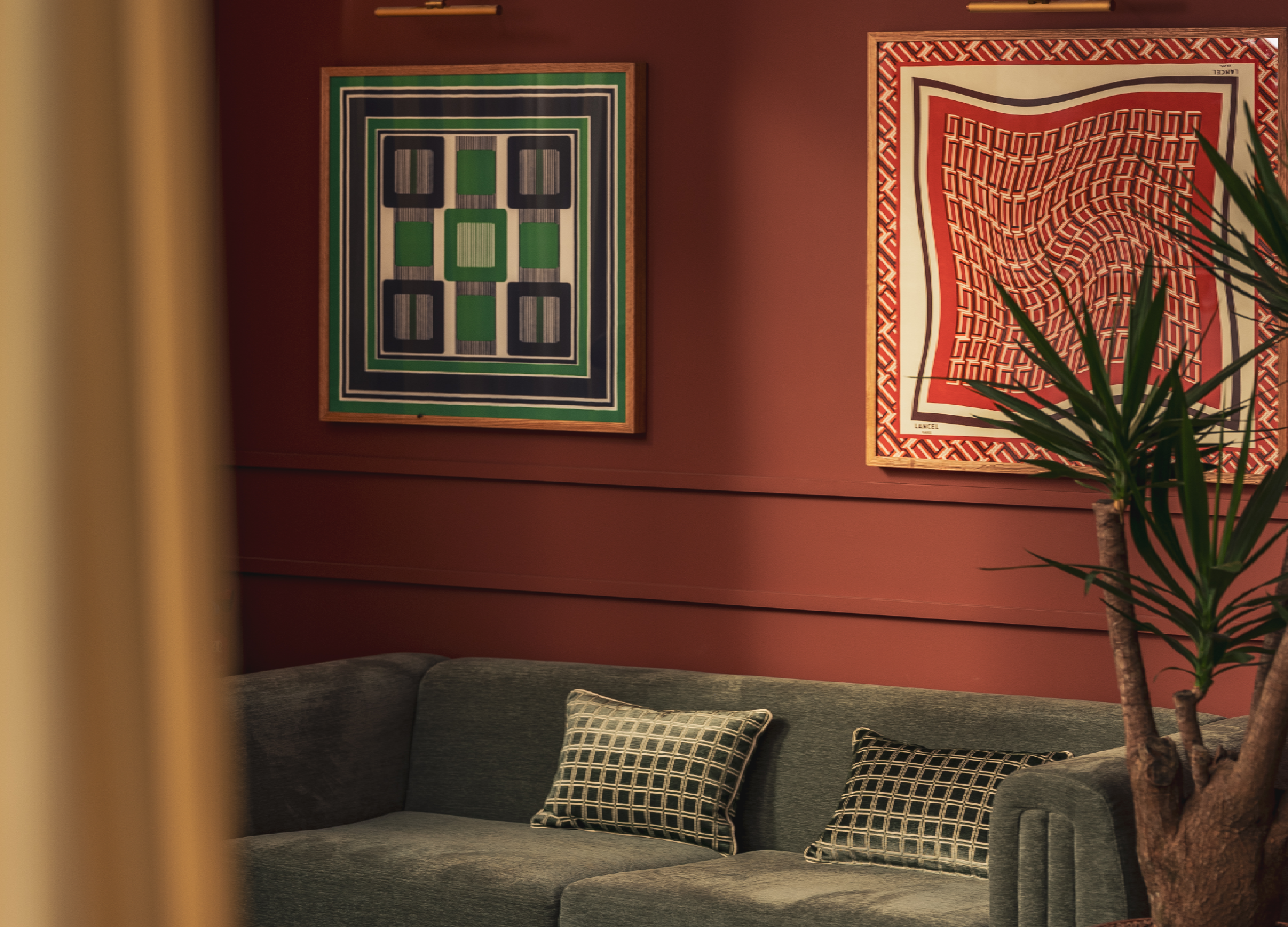 Living room with green sofa, square-patterned cushions and two geometric paintings on a red wall.
