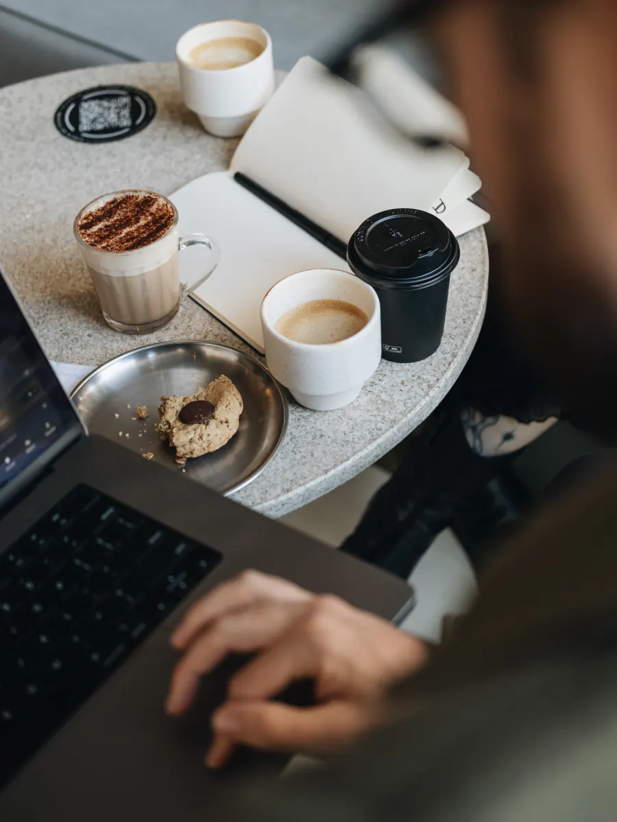Mesa de coworking com cafés, cookie, caderno e notebook na Offcina