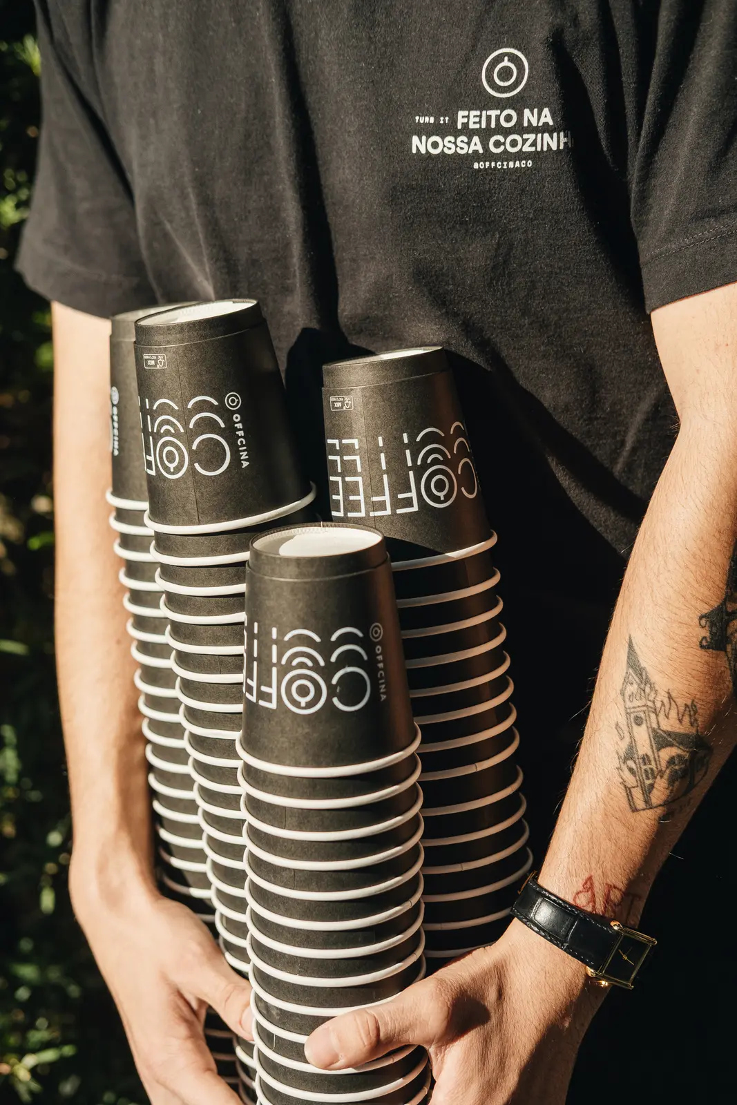 Barista da Offcina sorrindo enquanto carrega pilhas de copos de café da marca