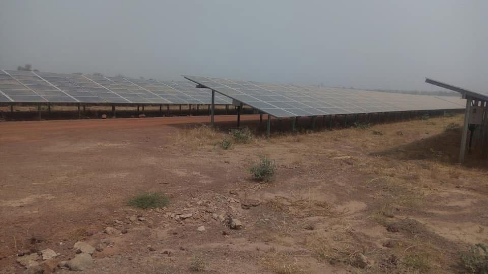 Rows of solar panels installed on a dry, rocky ground under a hazy sky.