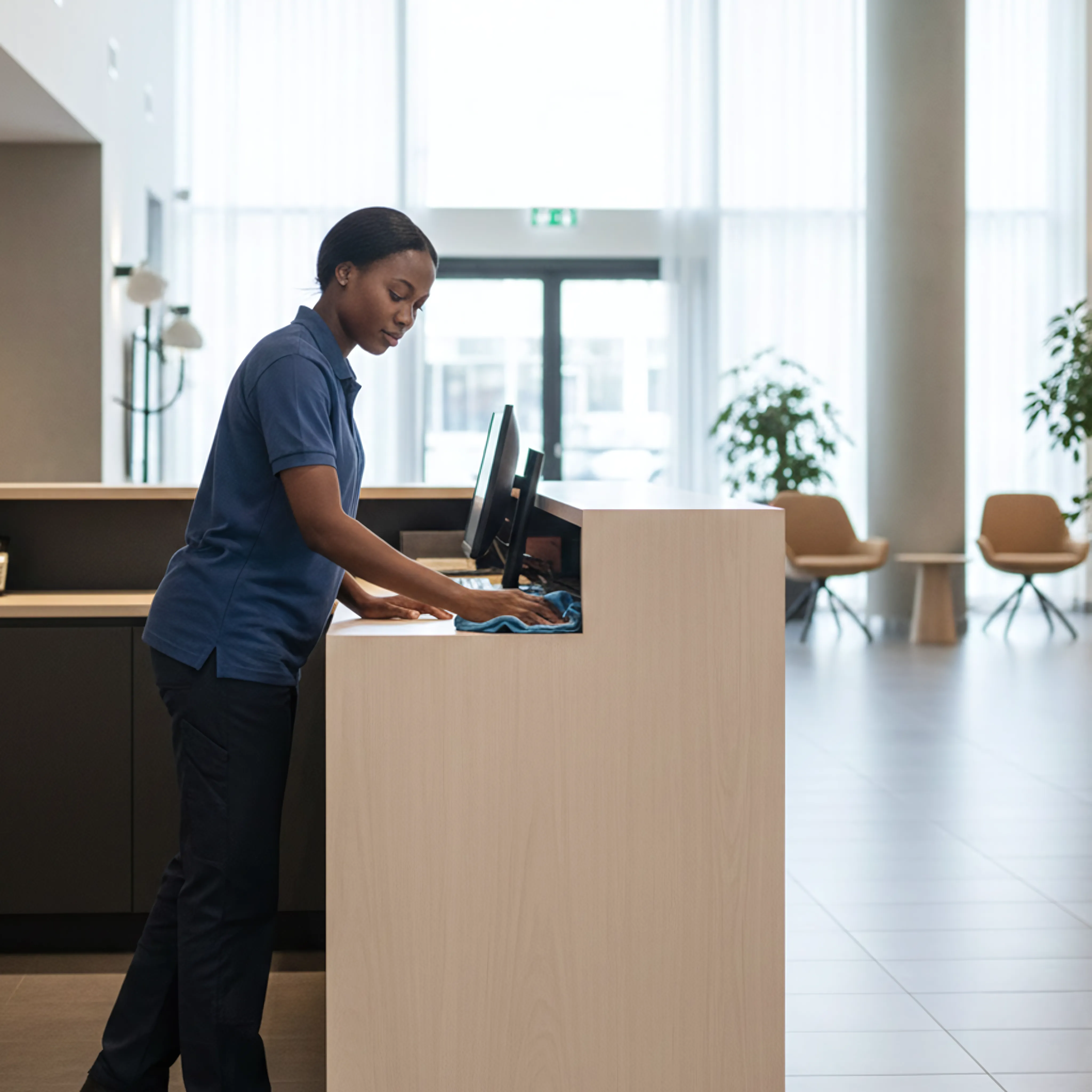 Schoonmaakmedewerker reinigt receptiebalie met microvezeldoek in een representatieve lobby