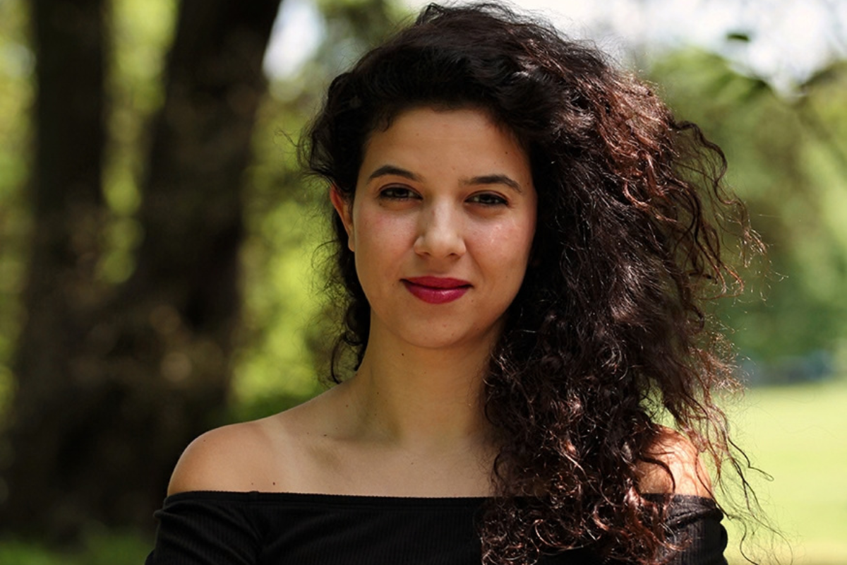 a professional headshot of the awardee- a woman with curly brown hair and big brown eyes. she has a soft smile and wears magenta lipstick