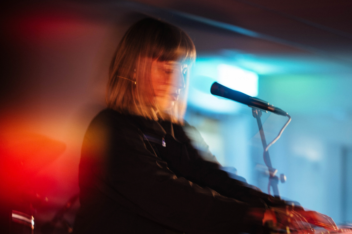 an atmospheric, neon-drenched photograph of a woman at a DJ deck